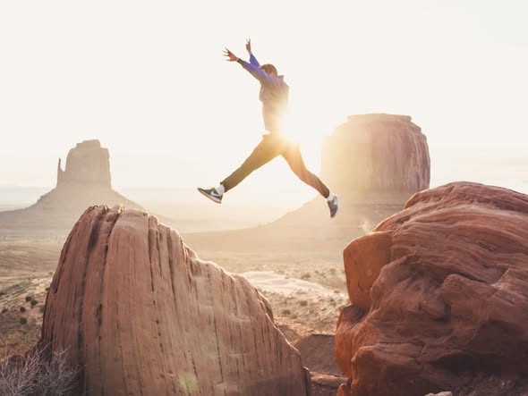 Homme sautant entre deux rochers au coucher du soleil dans Monument Valley